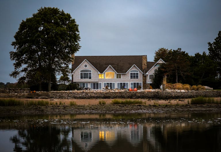 A picturesque waterfront home reflecting in calm water at twilight with warm interior lights.